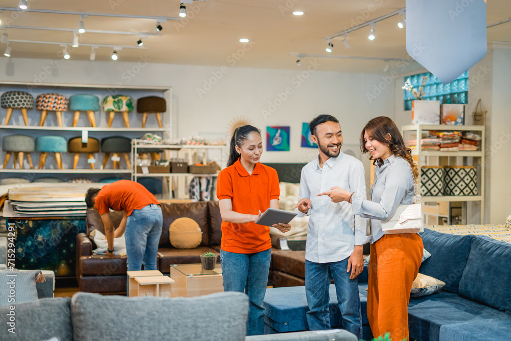 couple male and female customers chat with a female store employee while viewing products using a tablet in a furniture department store couple male and female customers chat with a female store employee while viewing products using a tablet in a furniture department store