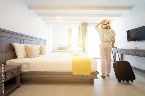 Rear view of young tourist woman looking to view outside window in hotel bedroom after check-in.