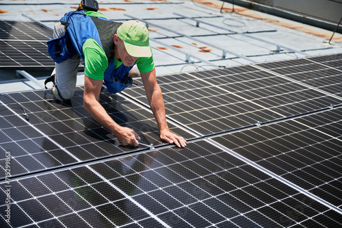 Worker building photovoltaic solar panel system on rooftop of house. Man engineer installing solar module with help of wrench outdoors. Alternative and renewable energy generation concept.