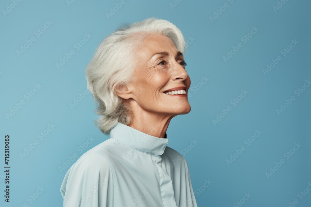 Cheerful senior woman looking away and smiling while standing against blue background Cheerful senior woman looking away and smiling while standing against blue background