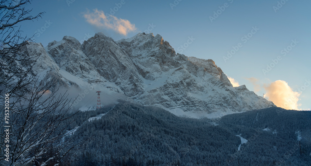 A bottom up view to the ice cold and with snow covered Zugspitze mountain chain and the surrounding forest nature landscape