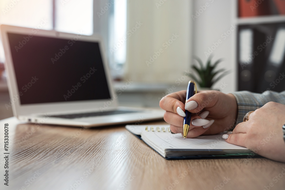 Fototapeta premium close up female hand making note on notepad with laptop, work at office or job freelance at home