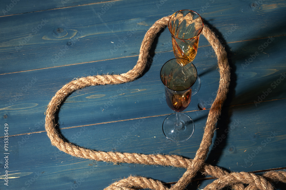 Naklejka premium Rope folded in the shape of a heart. Wine glasses on a wooden blue bridge. Valentines day template.