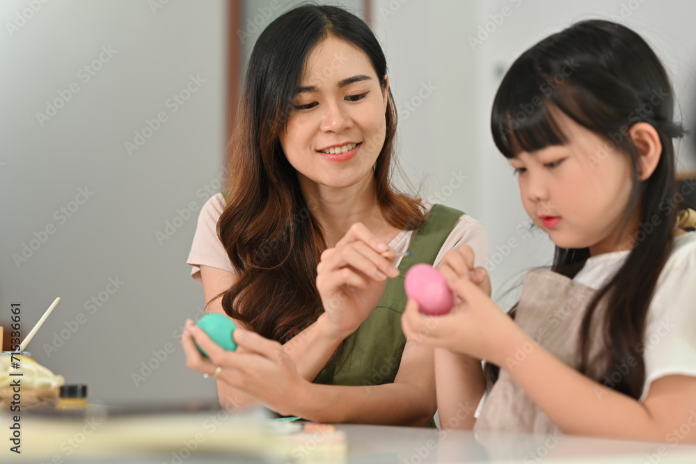 Smiling little girl painting Easter eggs with mother, getting ready for holiday at home Smiling little girl painting Easter eggs with mother, getting ready for holiday at home