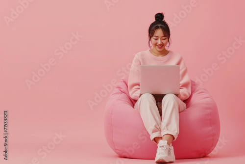 Full body young happy young woman of Asian ethnicity sit in bag chair use work on laptop isolated on plain pink background. AI generative