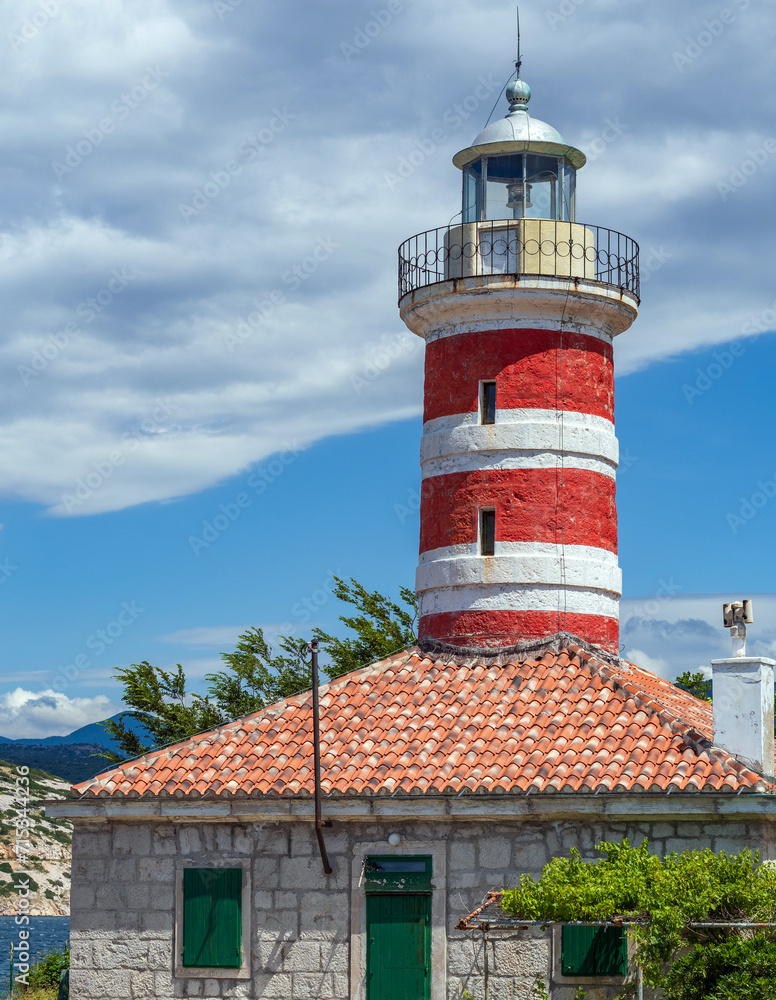 Picturesque stone house with red and white lighthouse against blue sky