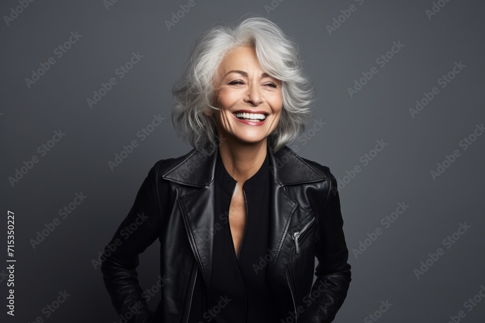 Portrait of smiling senior woman in black leather jacket, over grey background Portrait of smiling senior woman in black leather jacket, over grey background