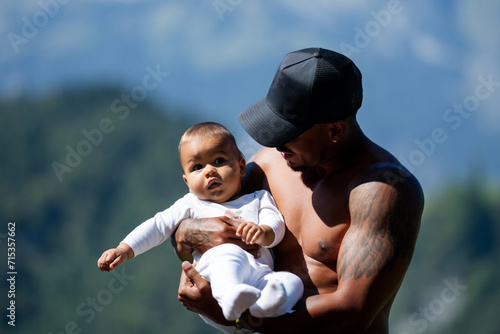 Close up portrait of afro american father kissing multiracial Biracial baby. Father hug Biracial child oudoor. Father with Biracial baby on nature. Hathers hand carrying Biracial baby. photo