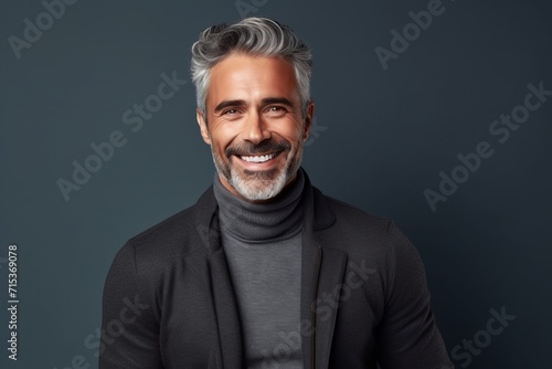 Handsome middle-aged man smiling at camera while standing against grey background photo