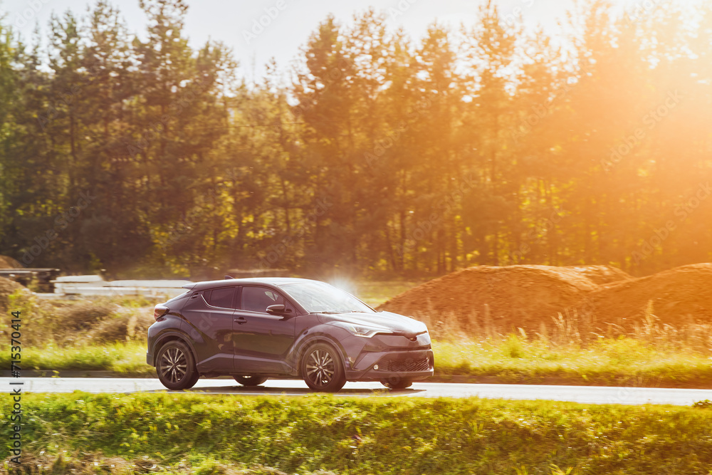 A hybrid SUV car journeys along a scenic road with majestic nature and a golden sunset in the backdrop.