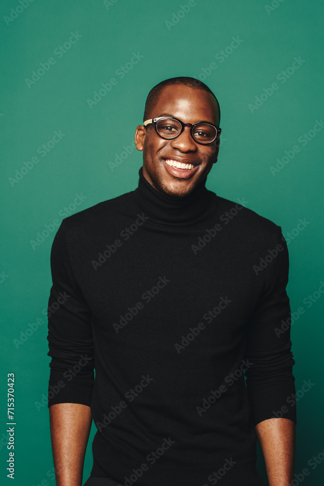 Confident young man with stylish glasses, smiling in casual attire on green background