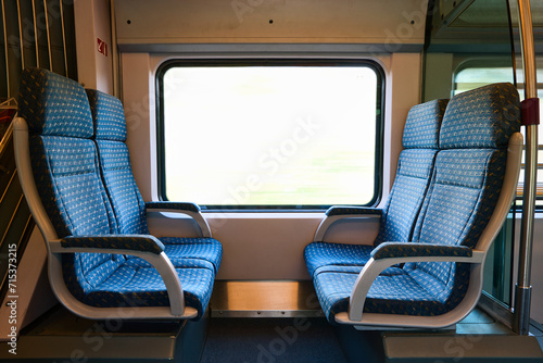 Empty blue seats in passenger train with bright window.