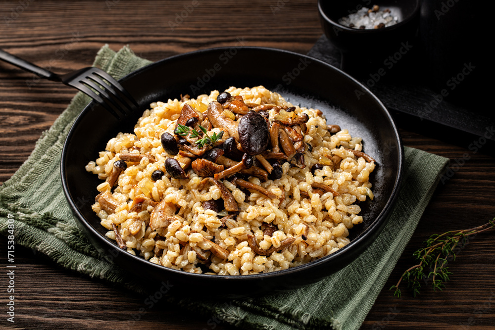 Mushroom barley risotto or orzotto in a black plate. Made with pioppini and porcini mushrooms. Vegan food. Mushroom barley risotto or orzotto in a black plate. Made with pioppini and porcini mushrooms. Vegan food.