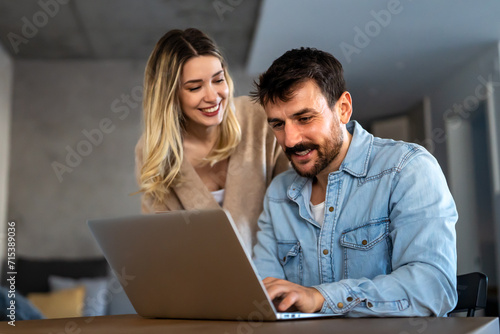 Cheerful young couple using laptop and smiling while shopping online at home