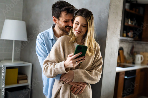 Young happy couple using phone to share social media news at home, doing shopping online.