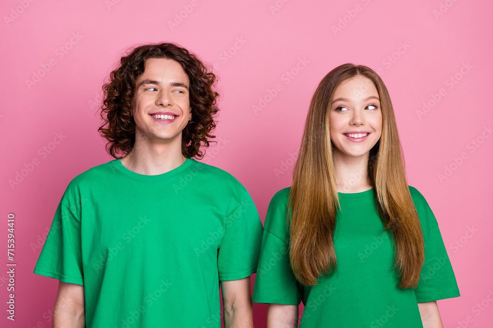 Photo of two positive teenagers wearing same color green t shirt couple smiling and look each other flirting isolated over pink background Photo of two positive teenagers wearing same color green t shirt couple smiling and look each other flirting isolated over pink background