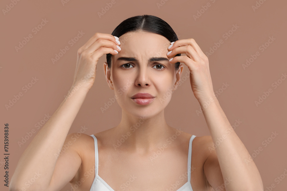 Fototapeta premium Woman with dry skin checking her face on beige background