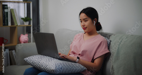 Portrait of Young woman sitting on sofa while working with laptop at home office.