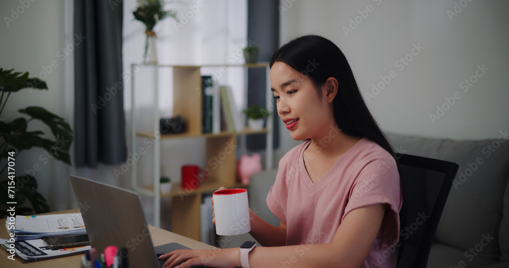 Portrait of Young woman holding coffee to drinking while working on the table in living room at home office.