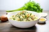 potato salad in white bowl with parsley, salt, and pepper shakers