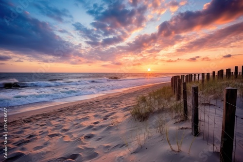  a sunset on a beach with a fence in the foreground and a body of water on the other side of the fence.