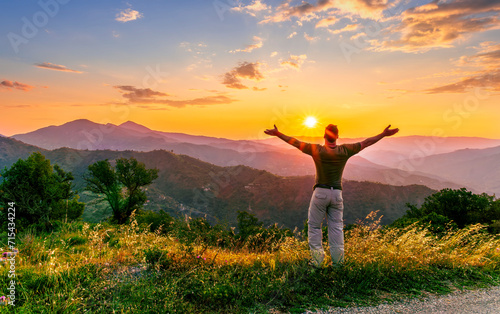 rejoicing man with beautiful scenic mountain sunset landscape on background. happy man watching amazing evening sunset