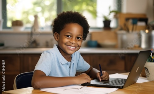 a small black boy working on his laptop computer at a desk with a smile