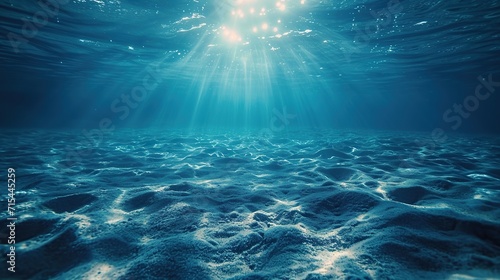 Sunlight pierces the clear blue waters of the ocean, illuminating the tranquil sandy sea floor below.