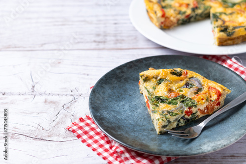 Italian Frittata made with spinach, tomatoes, onion and peppers on white wooden table. Copy space