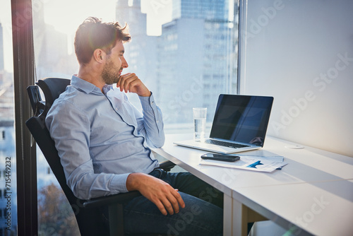 Thoughtful young businessman sitting with laptop at desk photo