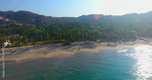 A close shot sliding by a gorgeous white sand beach with palm trees and calm teal water along the coast of Mexico photo