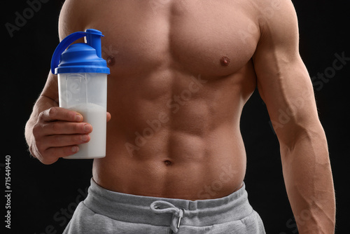 Young man with muscular body holding shaker of protein on black background, closeup