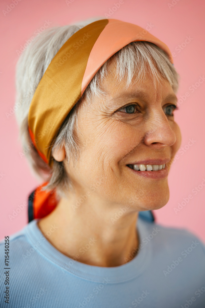 Smiling mature woman wearing bandana against pink background Smiling mature woman wearing bandana against pink background