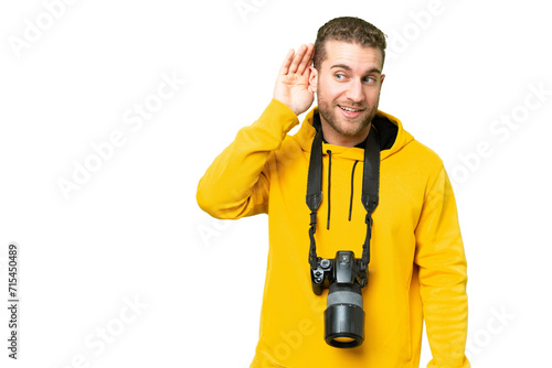 Young photographer man over isolated chroma key background listening to something by putting hand on the ear