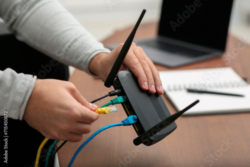Photography Man inserting cable into Wi-Fi router at wooden table indoors, closeup