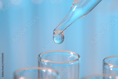 Laboratory analysis. Dripping liquid from pipette into glass test tube on light blue background, closeup