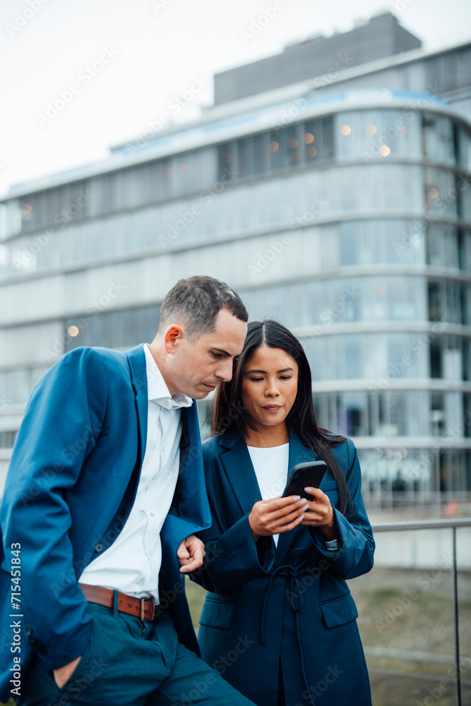 Businessman and businesswoman using smart phone in front of building Businessman and businesswoman using smart phone in front of building