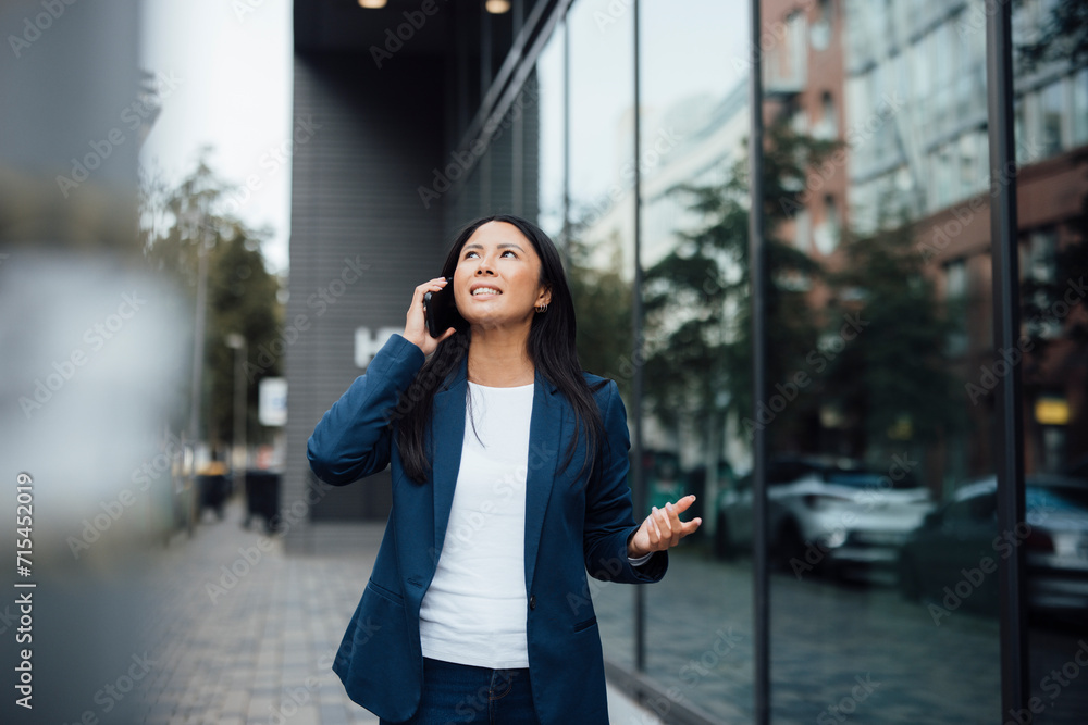 Smiling businesswoman talking on smart phone near building