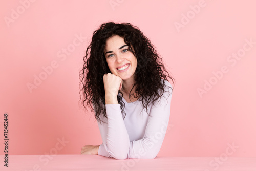 Smiling young woman sitting at table against pink background photo