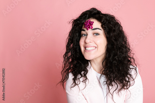 Happy young woman with tied bow on forehead against pink background photo