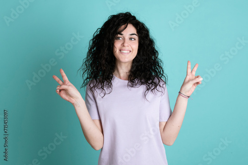 Smiling young woman gesturing peace sign against turquoise background photo