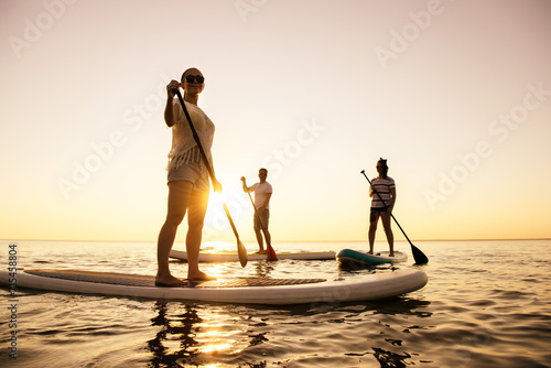 Three active young tourists are walking on standup paddle sup boards at sunset lake
