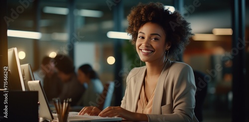 young professional smiling at computer working in open office.