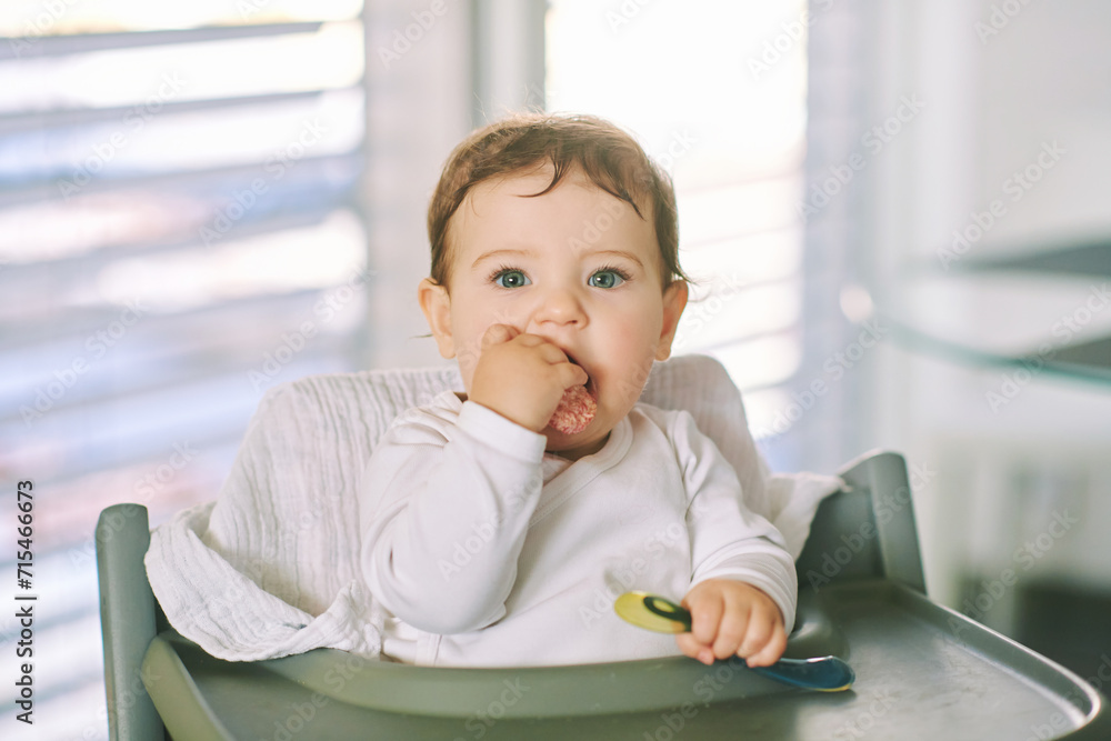 Portrait of adorable messy baby sitting in high chair, holding spoon Portrait of adorable messy baby sitting in high chair, holding spoon