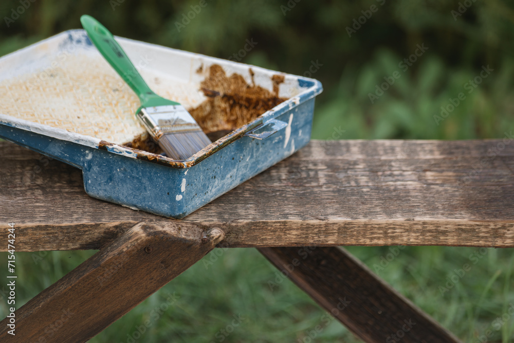 Protective varnish in a container, a brush on a wooden bench in the garden. Painting a wooden bench on a summer day in the garden. Protective varnish in a container, a brush on a wooden bench in the garden. Painting a wooden bench on a summer day in the garden.