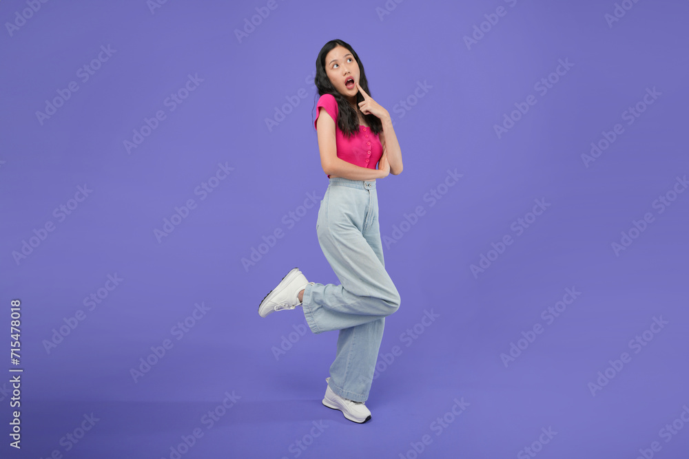 full body of a thoughtful Asian woman who keeps her hand on her chin and looks pensively above poses against a purple background blank copy space for your advertising content thinks about future full body of a thoughtful Asian woman who keeps her hand on her chin and looks pensively above poses against a purple background blank copy space for your advertising content thinks about future