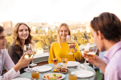 Cheerful friends drinking white wine during roof party