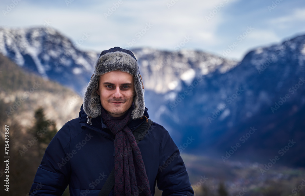 Young man in winter coat and hat with mountains in background Young man in winter coat and hat with mountains in background