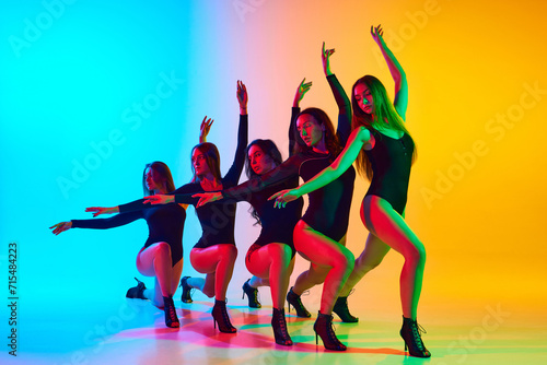 Artistic, expressive young women in black bodysuits dancing on high heels against gradient blue yellow background in neon light. Concept of modern dance style, creativity and beauty, art, hobby