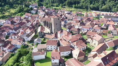 Scenic aerial view of spanish township of Isaba with brownish tiled roofs of residential buildings and medieval fortified church of Saint Cyprian in Roncal valley surrounded by green Pyrenees, Navarre photo